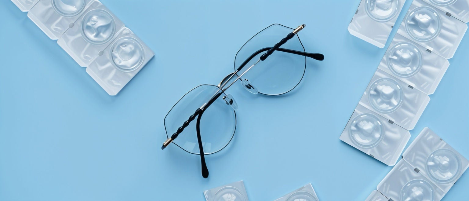 Paire de lunettes posée à côté de blisters de lentilles sur fond bleu