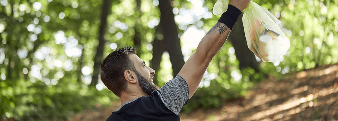 n joggeur lève un sac de déchets collectés en pleine nature, illustrant la pratique du plogging, un sport responsable qui allie course à pied et ramassage des déchets
