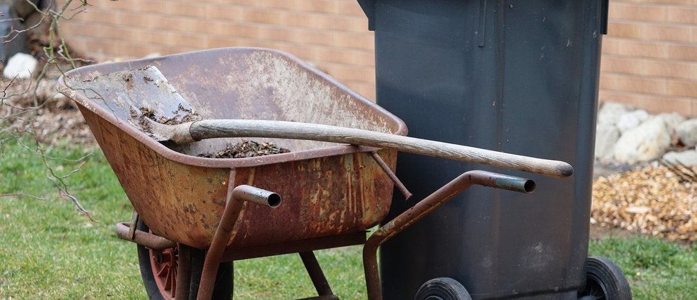 Une brouette métallique avec une poubelle en plastique marron dans un jardin