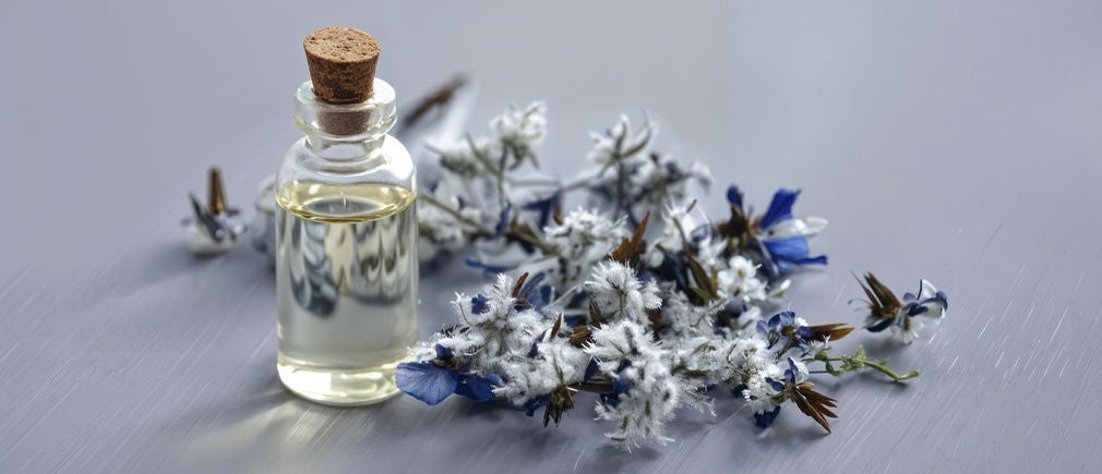 Flacon d’huile avec bouchon en liège entouré de fleurs blanches et bleues