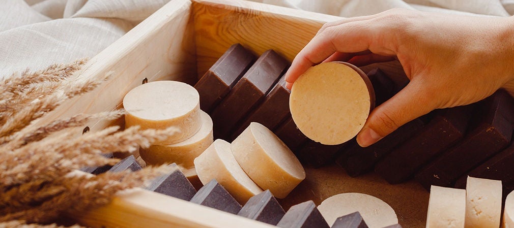 Main prenant un savon solide artisanal posé sur un support en bois