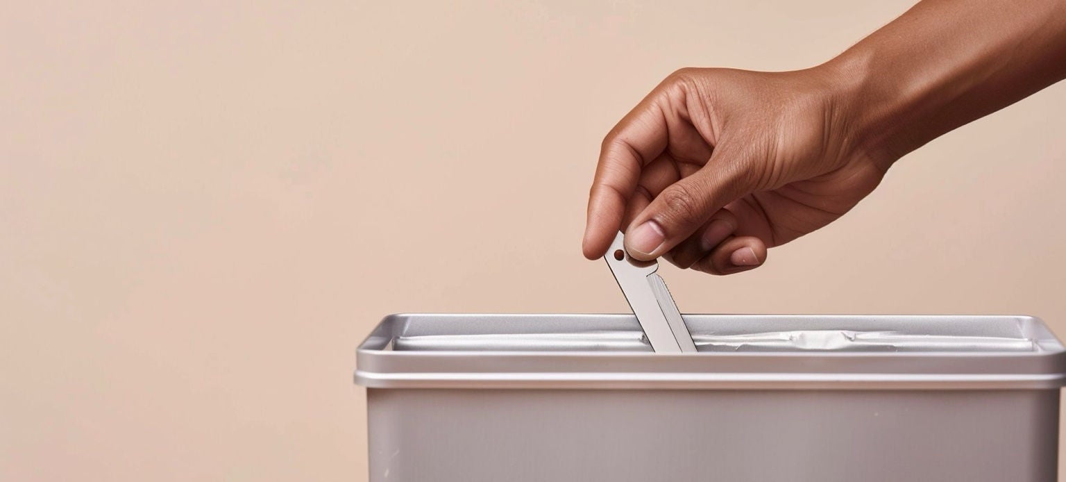 Main déposant une lame de rasoir usagée dans une poubelle métallique Handybag