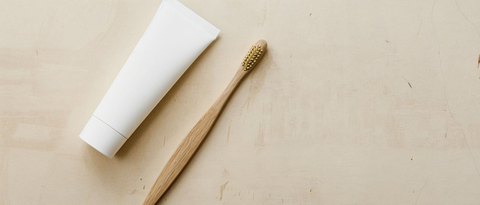 Tube de dentifrice blanc posé sur un fond beige à côté d’une brosse à dents