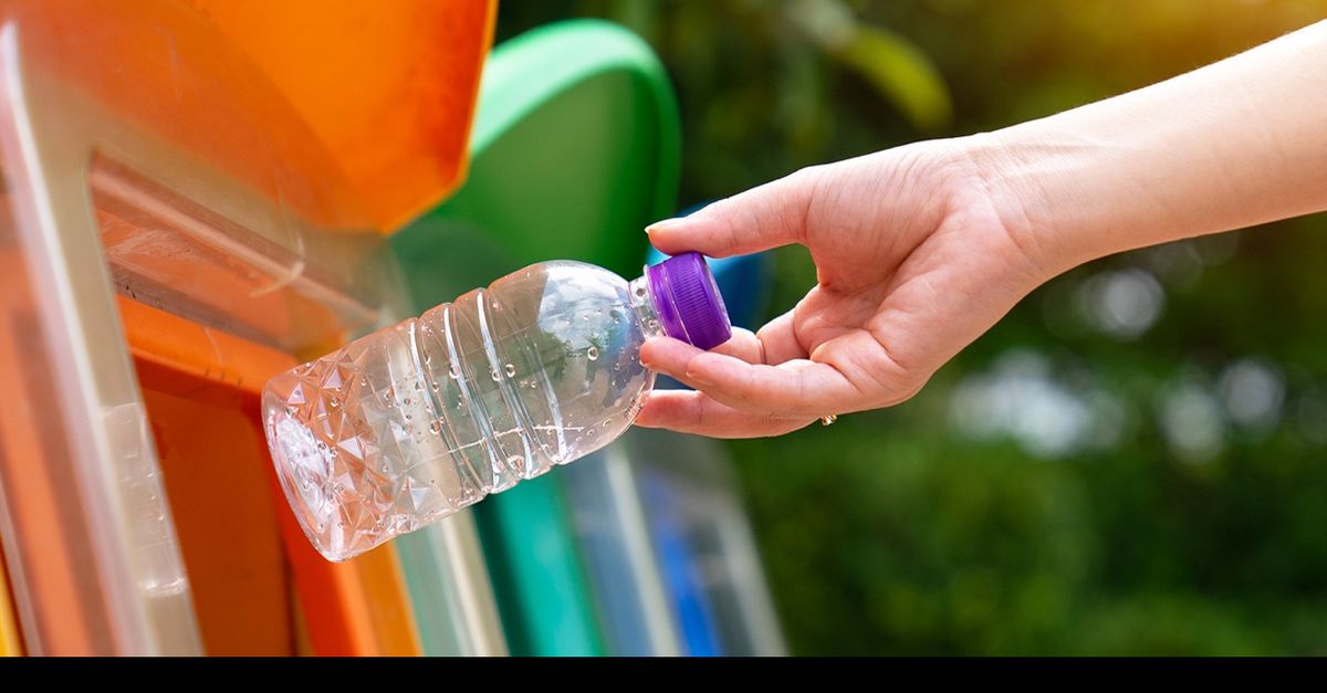 Une main dépose une bouteille d'eau en plastique dans un bac de recyclage coloré