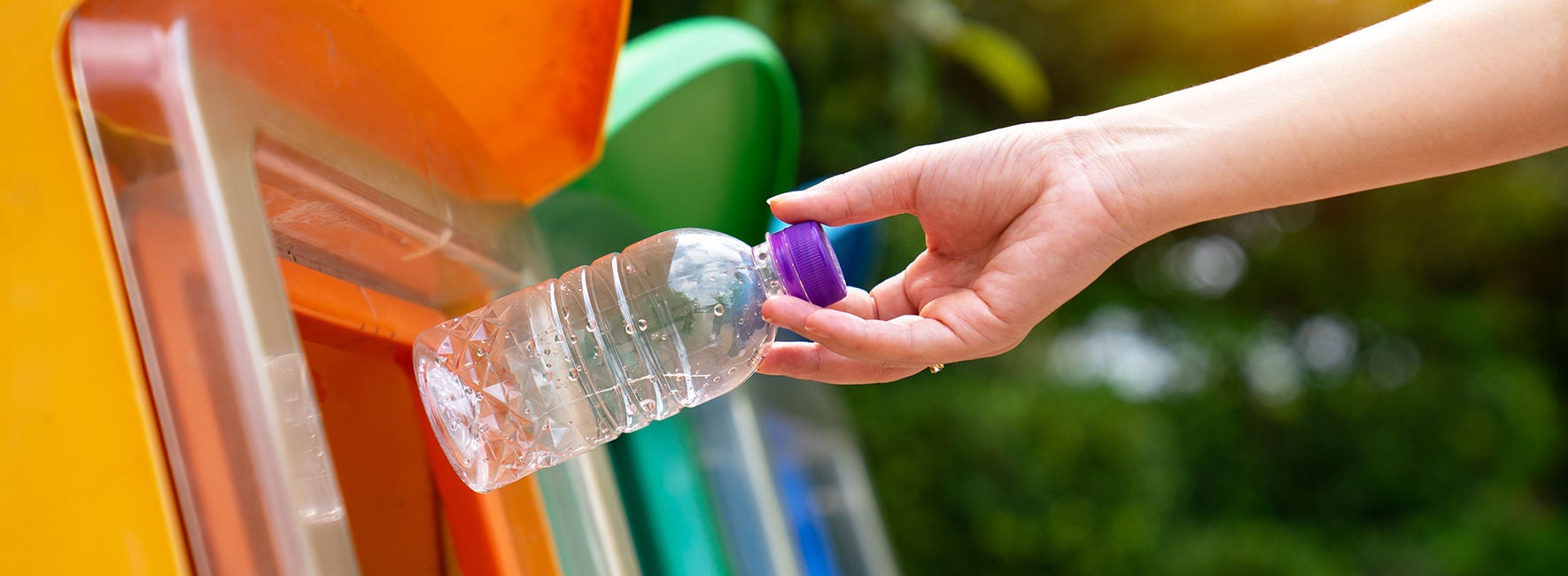 Main d'une personne jetant une bouteille en plastique dans une poubelle de tri sélectif