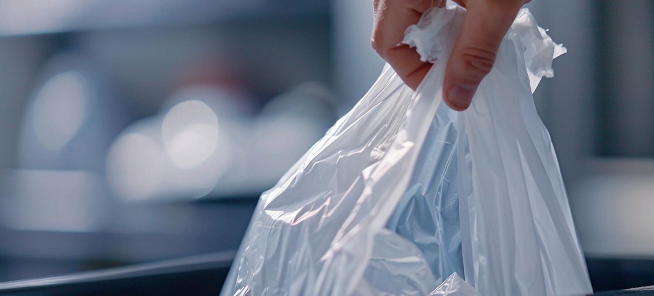 Une main dépose un sac plastique blanc rempli de déchets dans une poubelle, illustrant le geste du tri et de l’élimination des déchets ménagers 