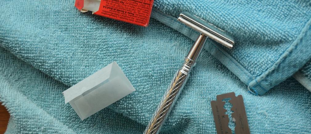 Rasoir de sûreté en métal posé sur une serviette bleue avec une lame et son emballage